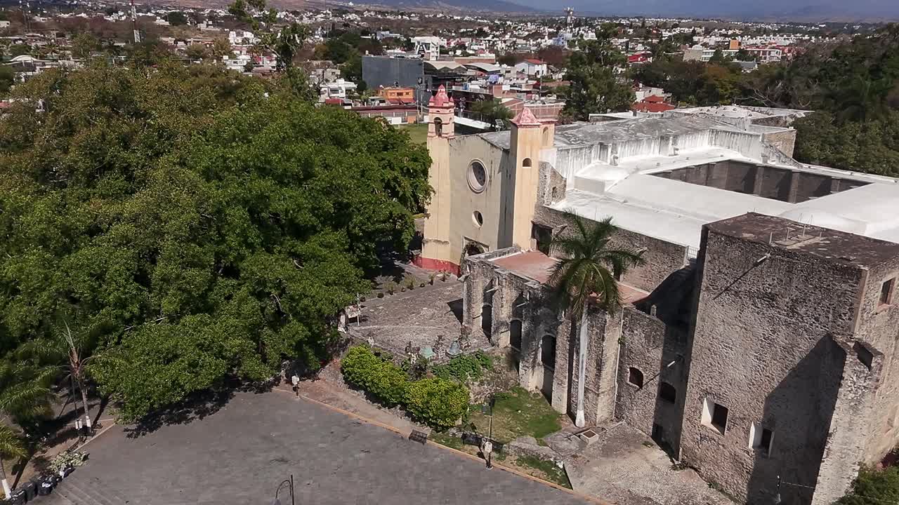 Old stone colonial church and lush plaza in Tlayacapan, Morelos, Mexico. Aerial drone static shot
