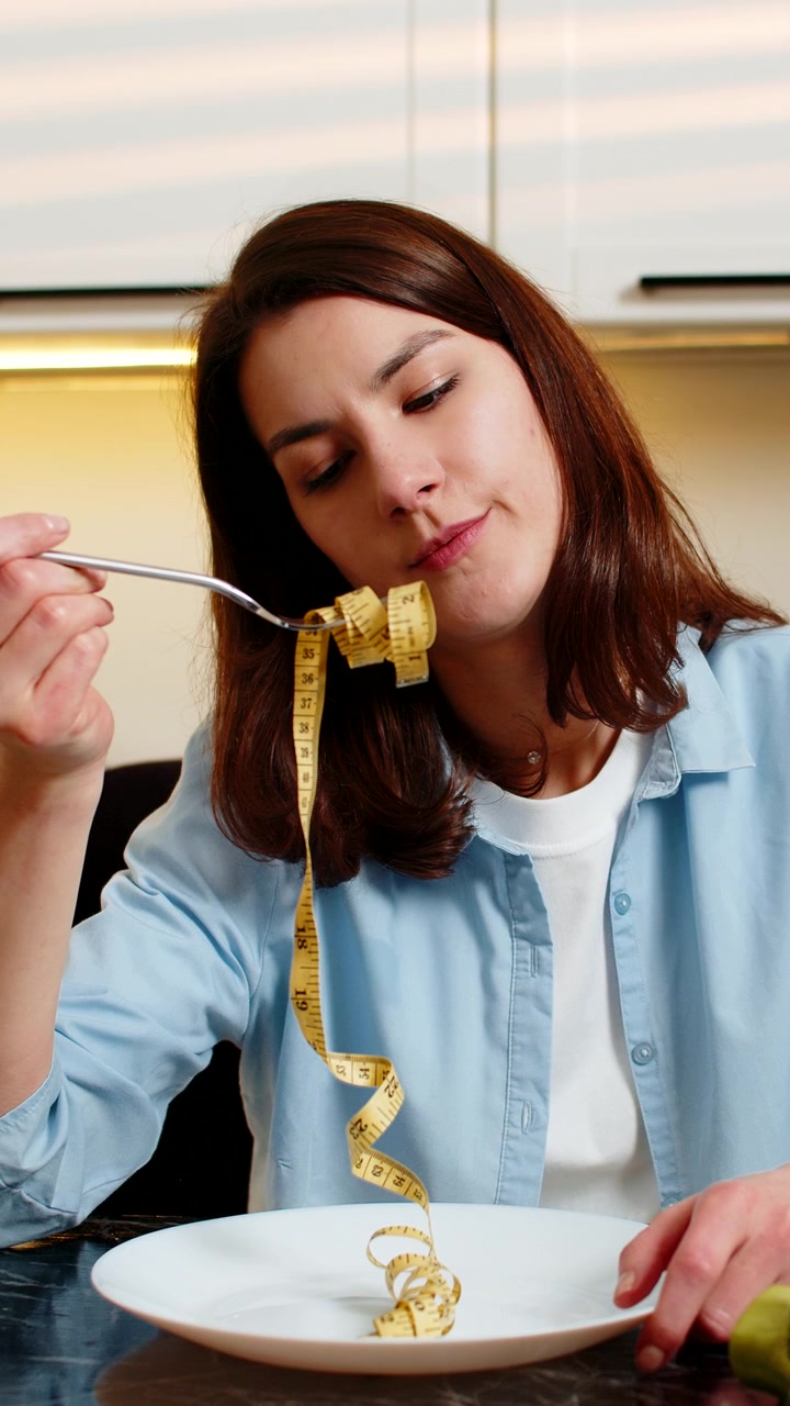 Young woman disappointed checking measuring tape during diet struggle weight loss at home in kitchen