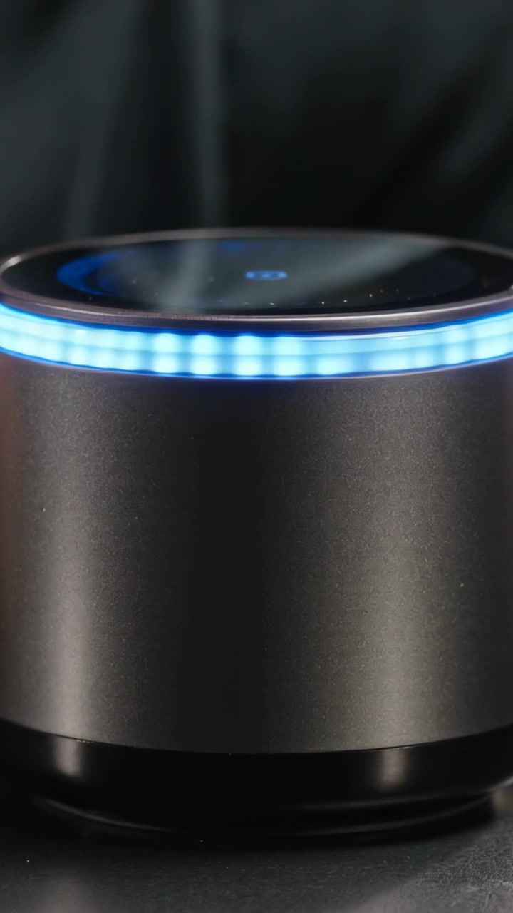 Video verticale: Una persona si china e parla vicino a un cilindro su un tavolo per attivare un anello LED blu e vapore.