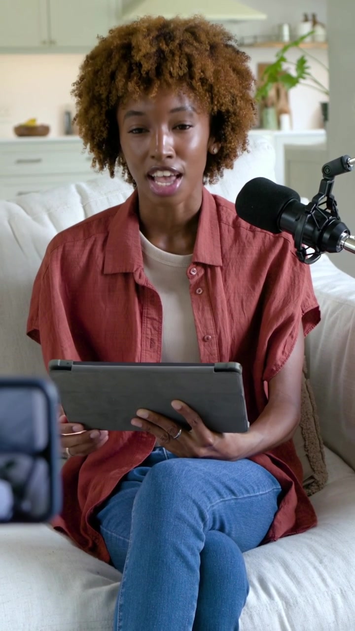 Vertical video: Starting reading tablet, host in shirt filming on sofa, gesturing at mic