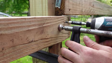 Using metal clamp and cordless power drill to build wooden fence, close up