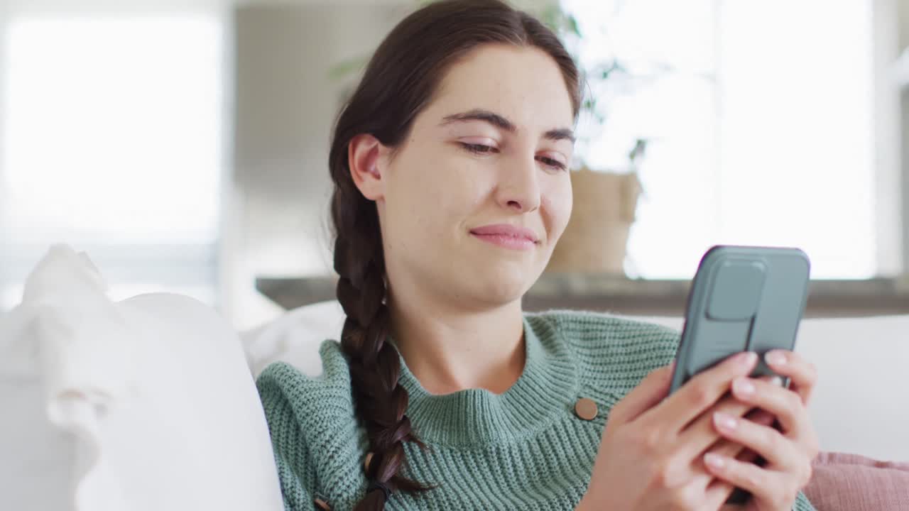 mujer caucásica feliz sentada en el sofá y enviando mensajes de texto en el teléfono inteligente