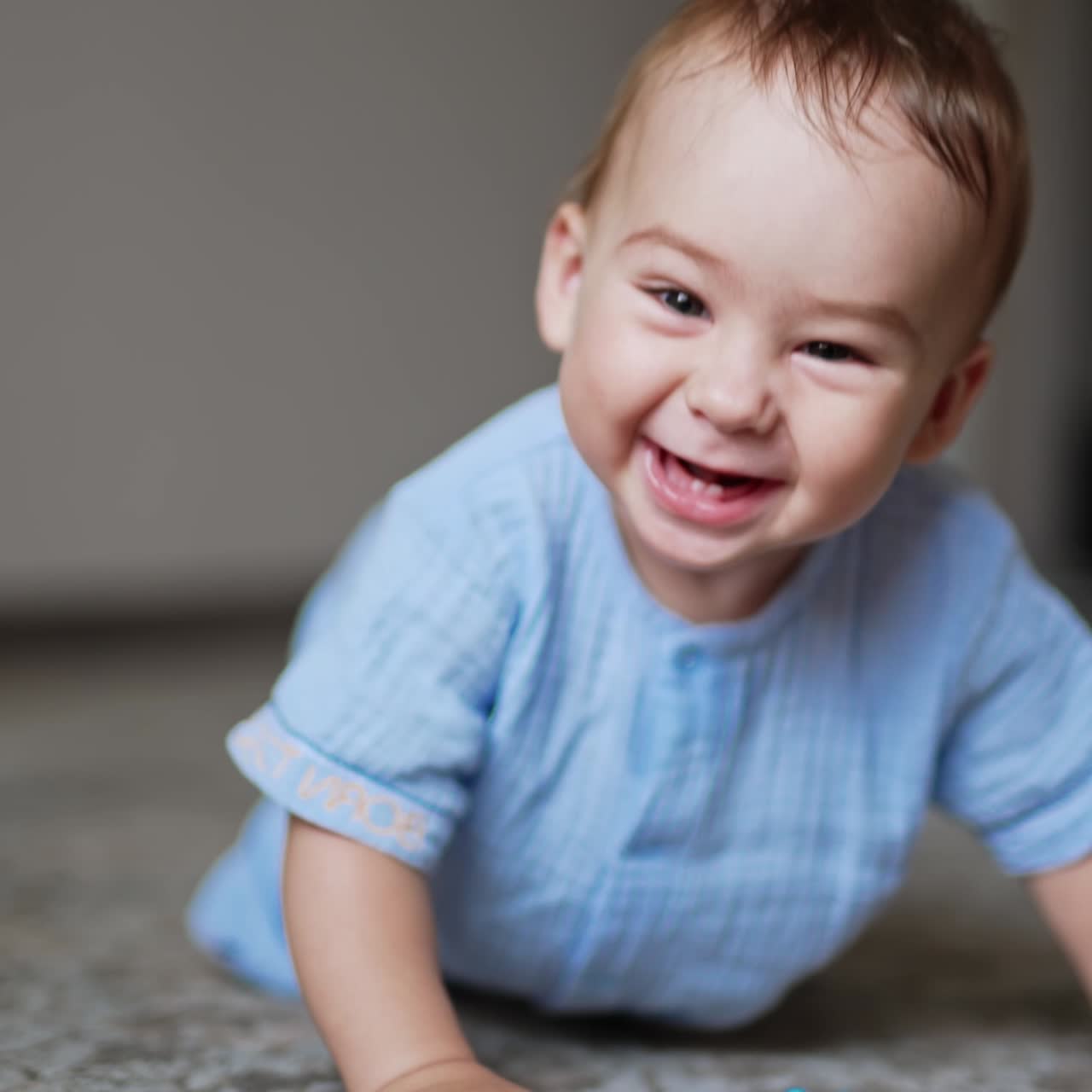 Adorable cheerful laughing toddler standing on all fours on the floor and swaying. Little kid playing with a toy