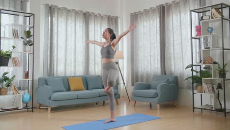 joven atlética asiática en ropa deportiva haciendo yoga en la postura del árbol en la alfombra en casa