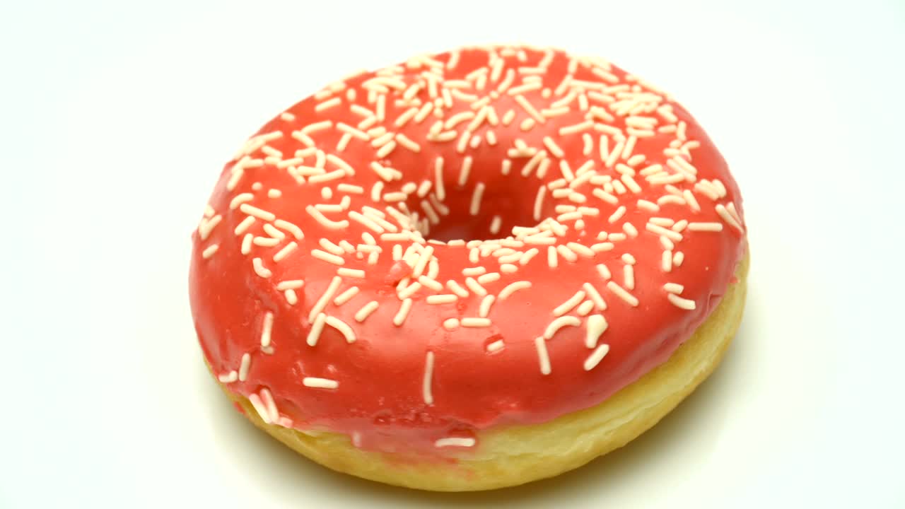 deliciosa rosquilla roja dulce girando en un plato. vista lateral. rosquilla salpicada brillante y colorida macro disparo de primer plano girando en una placa blanca.