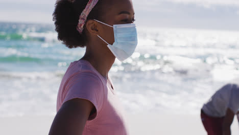 african american couple wearing face masks collecting rubbish from the beach