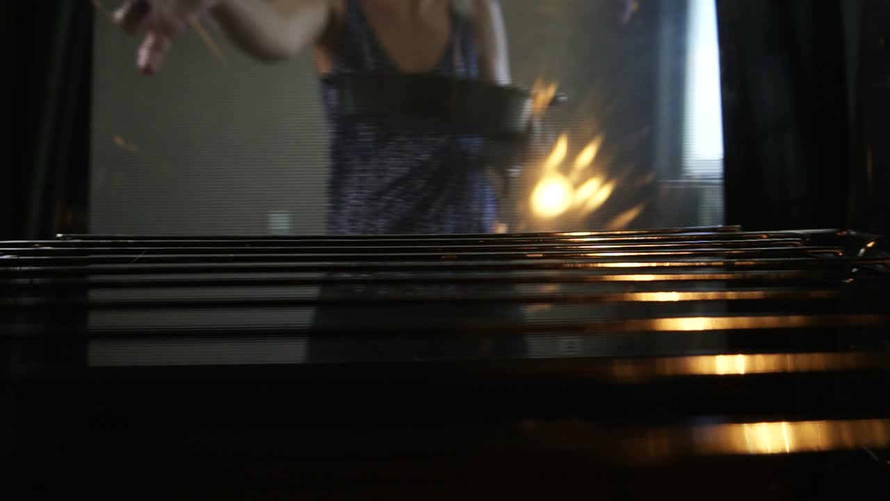 Close Up view of woman's hands taking out a baking pan from the oven and closing the oven's door. View from the oven. Homemade