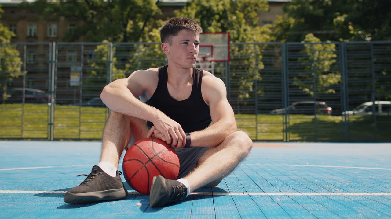 Tired athletic caucasian man in sportswear relaxing after playing basketball game listening music