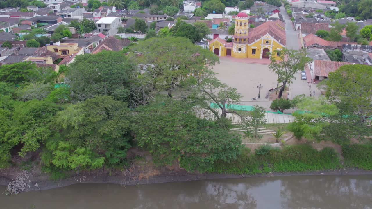 The drone begins low over the calm waters of the Magdalena River, capturing its gentle ripples reflecting the morning light. As it reveals the stunning silhouette of Santa Barbara Church.
