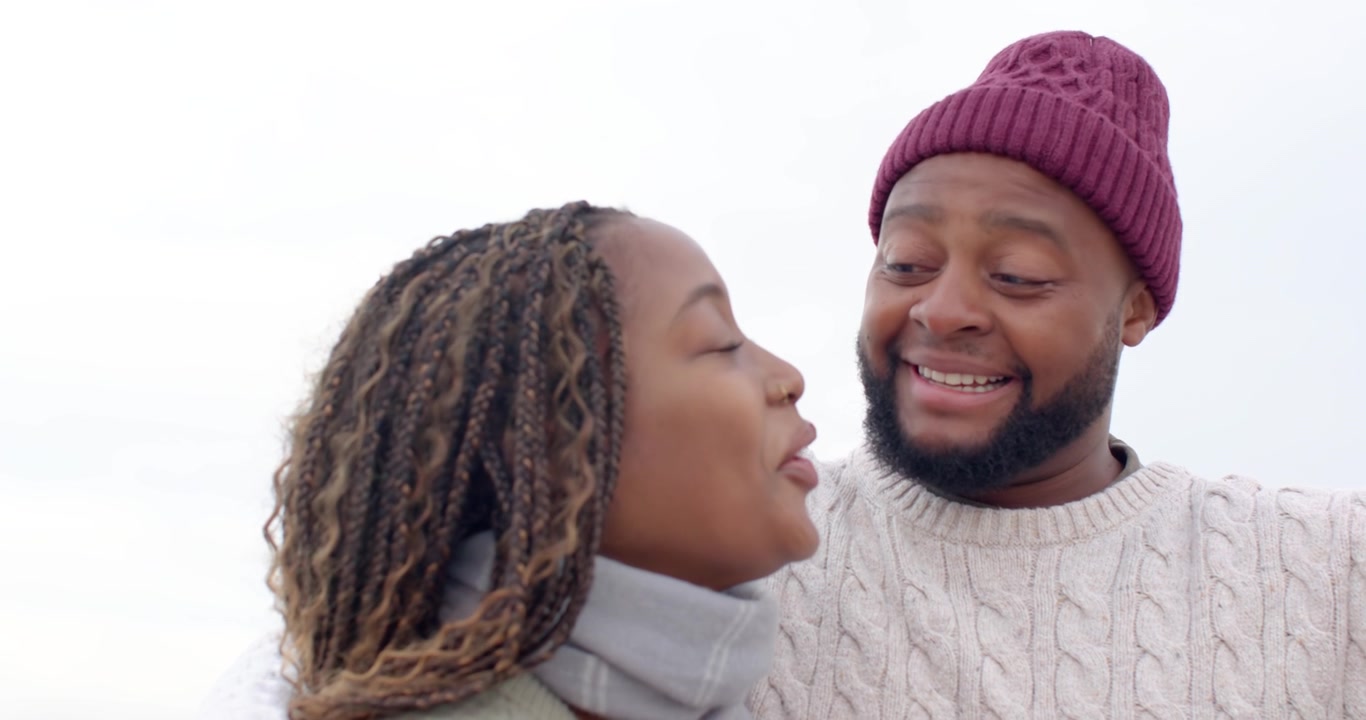 Couple talking his arm around her shoulder showing affection knit sweaters scarf beanie by sea