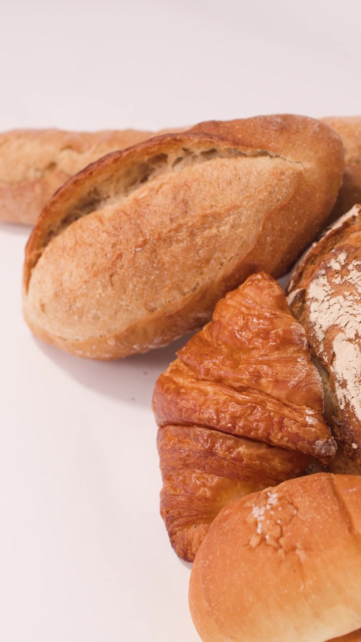 La telecamera si muove su pane a lievitazione naturale dorato, baguette francesi e croissant su uno sfondo bianco pulito.