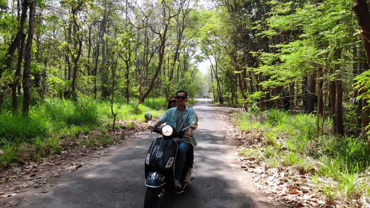 시골 도로 를 따라 모터 스쿠터 를 타고 있는 젊은 부부