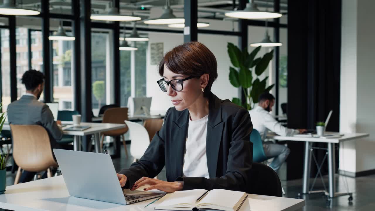 Scena video professionale di un ufficio con un angolo laterale che cattura una donna concentrata con gli occhiali che lavora