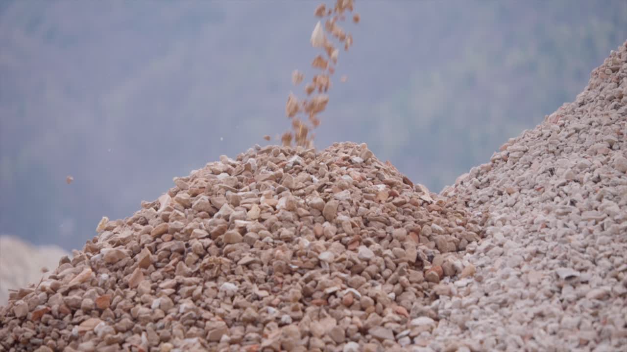 Close-up view about the falling and being poured chopped rocks debris in mining quarry.