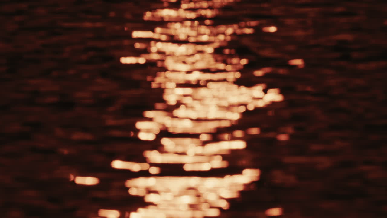 Närbild av orange och gyllene solnedgångsreflexer som rör sig över mjuka vattenkrusningar