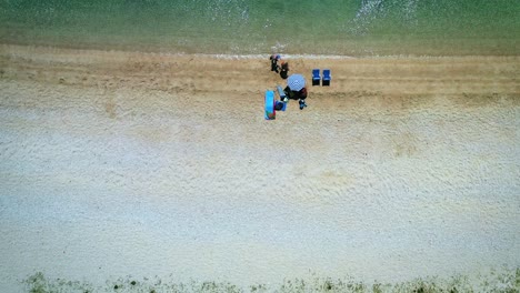 Pareja-En-La-Instalación-Junto-Al-Mar-Con-Sombrilla-Y-Sillas-De-Playa-Toma-Aérea-4k