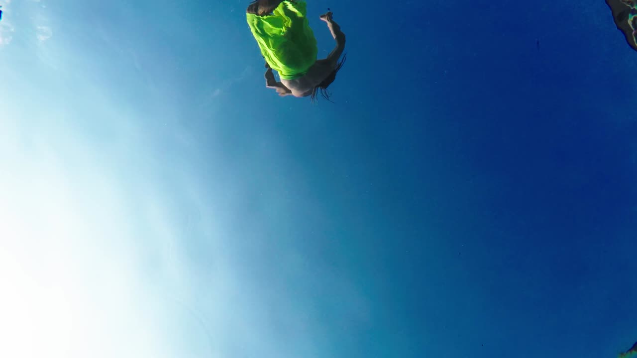 Giovane uomo atletico in pantaloncini gialli salta e si tuffa in piscina, ripresa dal basso.