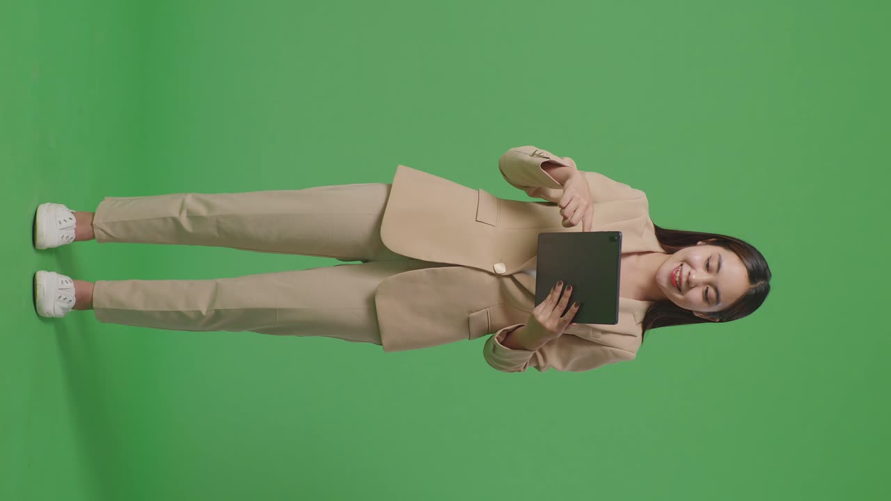 cuerpo lleno de mujer de negocios asiática sonriendo mientras usa la tableta en el fondo de la pantalla verde en el estudio