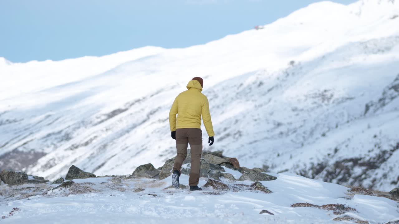 노란색 재킷을 입은 백인 청년과 비니를 걸고 스위스 플루엘라 패스에 있는 산골짜기의 전망을 보기 위해 멈춥니다
