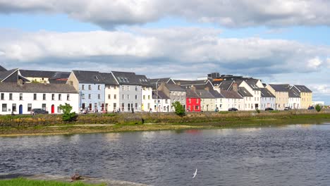 Bonitas-Casitas-De-Diferentes-Colores-A-Lo-Largo-De-La-Orilla-Del-Río-Con-Pájaros-Volando,-Galway