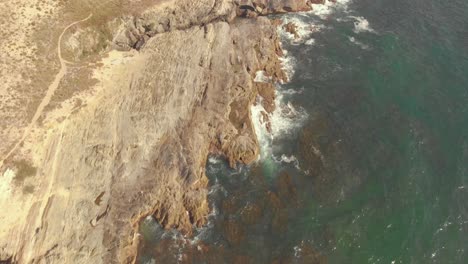 Flying-over-the-coast-line-in-Porto-Covo,-Portugal,-on-a-bright-day-but-with-haze-clouds-over-the-water