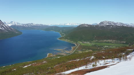 Aerial-view-overlooking-a-village-and-a-road,-on-the-coast-of-the-Barents-sea-,-revealing-a-huge-rock,-sunny,-summer-day,-in-Rotsund,-Troms,-Nordland,-Norway---reverse,-drone-shot