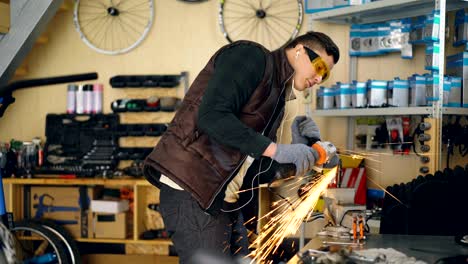 maintenance man is using electric circular saw while working in his small workplace. young man is wearing protective glasses and gloves and is listening to music with earphones.