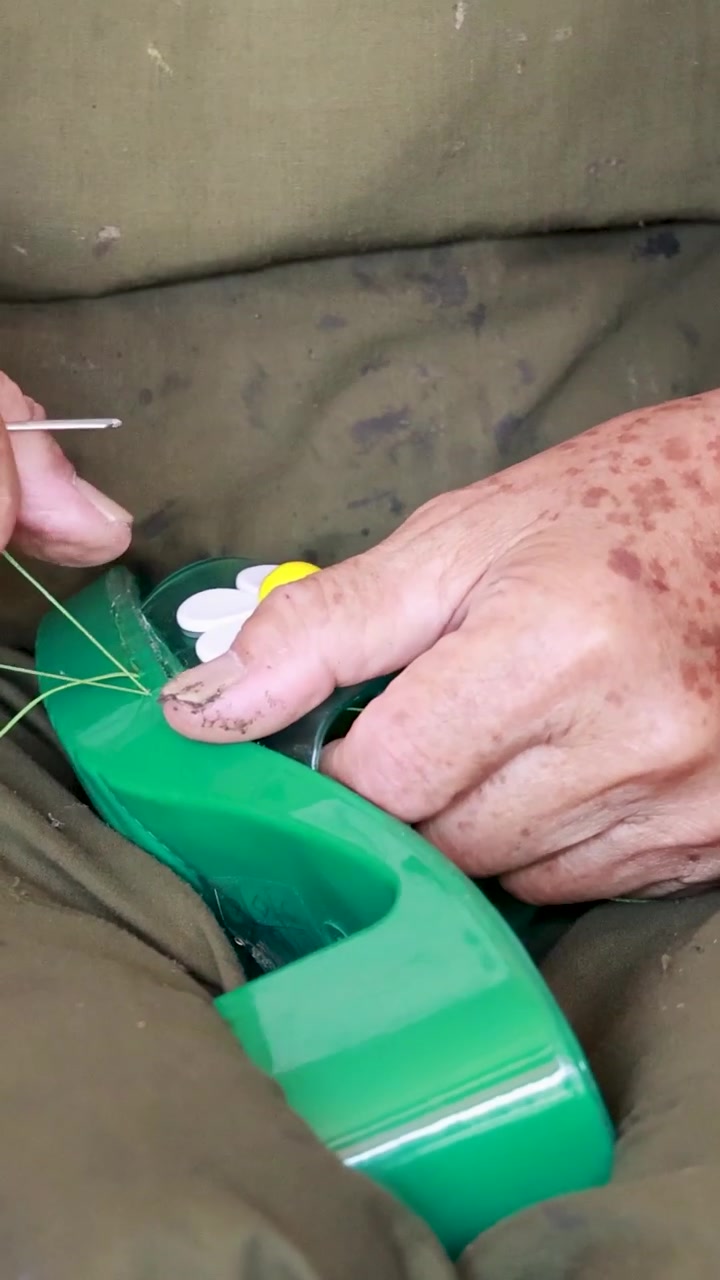 Skilled hands meticulously sew a green floral shoe using traditional needle and thread techniques.