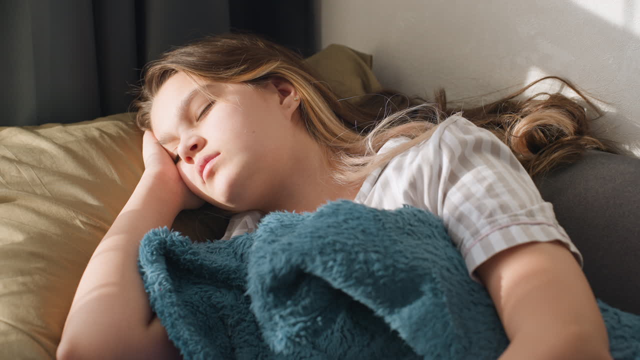 Young Woman Dozing With Cozy Blanket, Female University Student Peacefully Napping Under Soft Sunlight, Brightly Lit Scene Featuring Student Resting After Studying With Comforting Teal Blanket