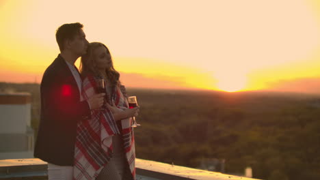 Loving-couple-is-sitting-on-the-roof-of-the-house.-In-the-distance-the-lights-of-the-night-city.