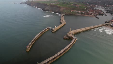 Toma-Aérea-De-Los-Faros-De-Los-Muelles-Este-Y-Oeste-De-Whitby-Y-Las-Balizas-De-Entrada-Del-Puerto-En-El-Centro-Turístico-Histórico-De-Whitby,-Yorkshire-Del-Norte,-Inglaterra