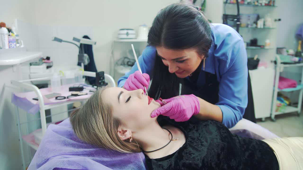 Makeup master in a beauty salon draws a lip contour to a girl. Permanent makeup procedure