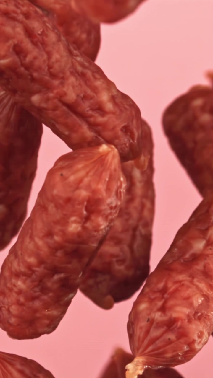 Primo piano di mini salamini appesi su sfondo rosa