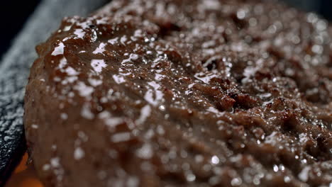 sizzling beef burger being grilled on smoking and flaming grill grate in macro