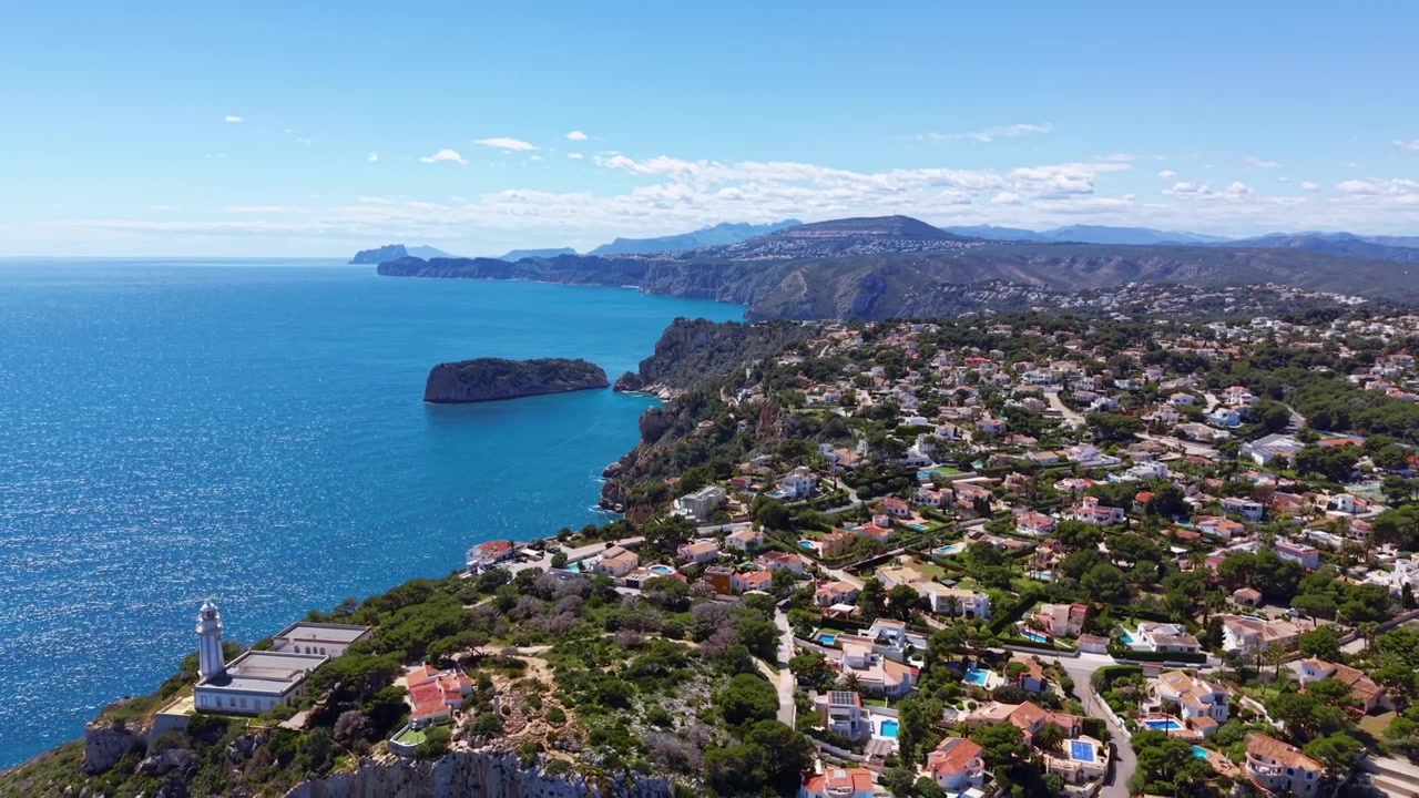 Vista panoramica della costa spagnola della Costa Blanca con acque turchesi del Mediterraneo, scogliere calcaree, un faro e ville residenziali immerse nel verde lussureggiante sotto un cielo azzurro e limpido