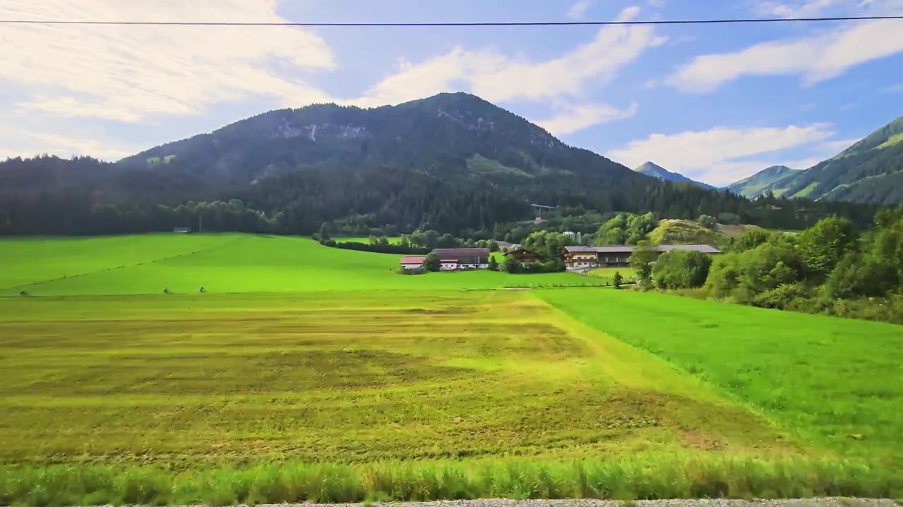 オーストリアでの美しい鉄道の旅。晴れた日に、広々とした牧草地、アルプスの村々、森林に覆われた丘、そして山々の景色が窓の外を流れていく。
