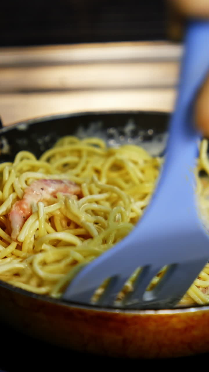 Man`s hands with kitchen spatula mixes pasta with sauce in frying pan. Selective focus. Tasty dinner. Vertical video
