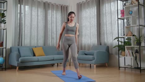 vista completa de una joven entrenadora asiática femenina en ropa deportiva hablando y haciendo yoga en postura de lanzamiento alto mientras enseña ejercicios en casa