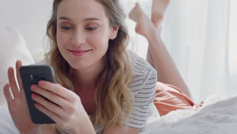 mujer hermosa usando un teléfono inteligente enviando mensajes de texto navegando por los mensajes de las redes sociales disfrutando de la comunicación por teléfono móvil acostada en la cama en casa