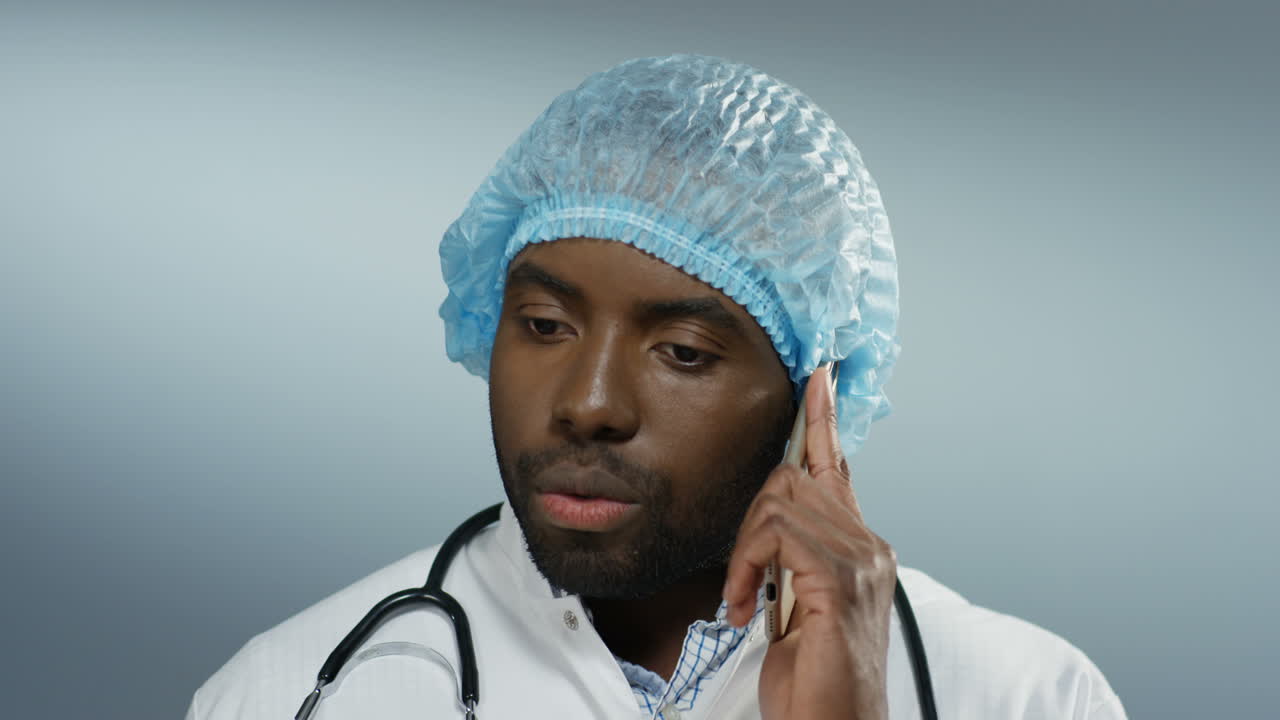 joven apuesto médico con sombrero y con un estetoscopio en diablos hablando por teléfono móvil y resolviendo algún problema y diciendo cómo tratar