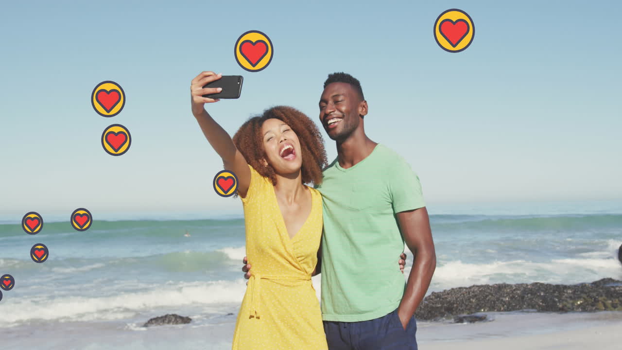 animación de los iconos del corazón de las redes sociales sobre una pareja sonriente tomando una selfie con un teléfono inteligente en la playa