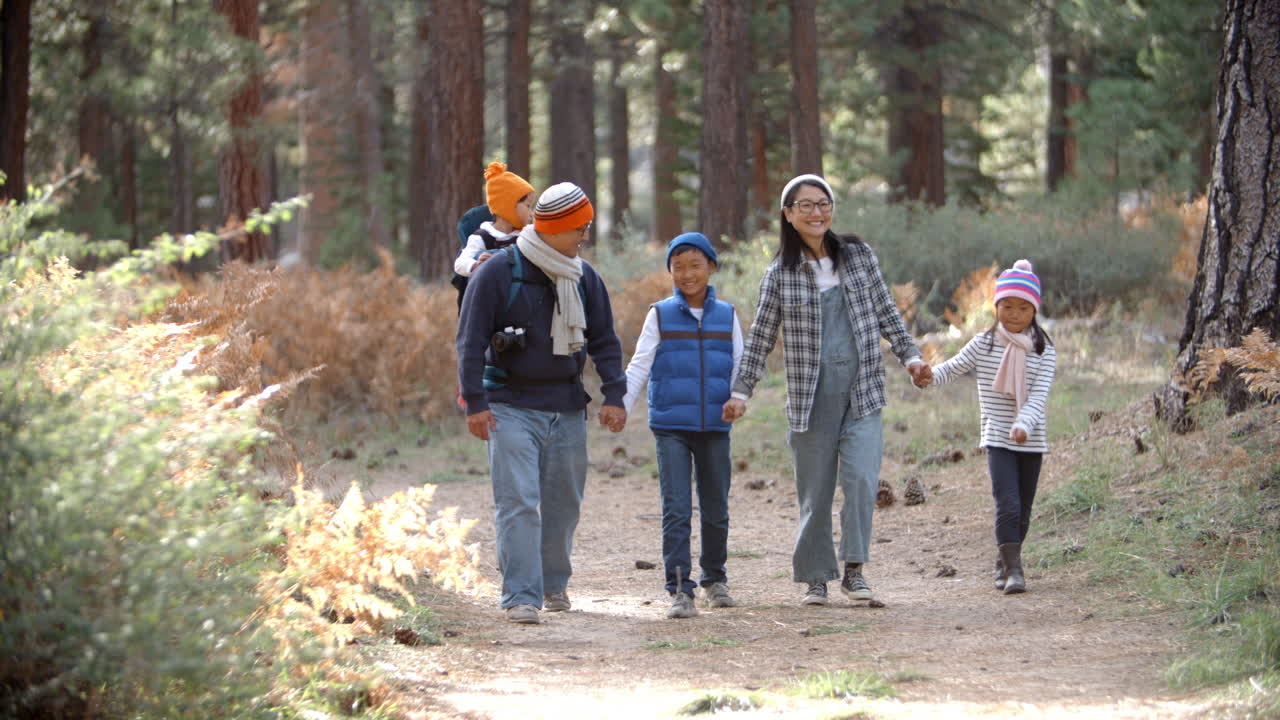 Asiatisk familie går mot kameraet i en skog, sett forfra.