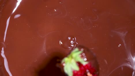 strawberry being dipped and lifted from chocolate