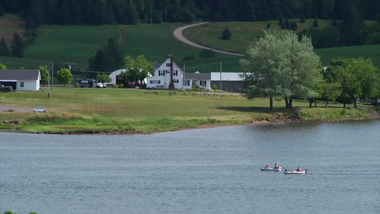 Two small boats gently sail by a farm house on the Bouctouche River near Sainte-Marie-de-Kent in New Brunswick, Canada