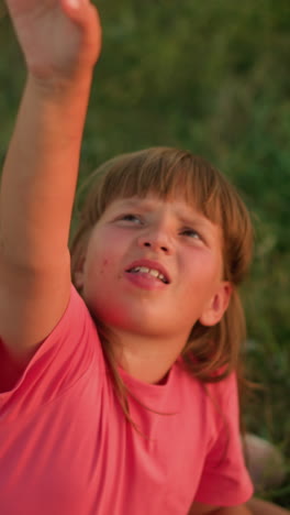 joven con camiseta rosa sentada al aire libre alcanzando alegremente hacia burbujas flotantes con curiosidad lúdica, rodeada de configuración de picnic con rebanadas de sandía, vegetación natural y canasta