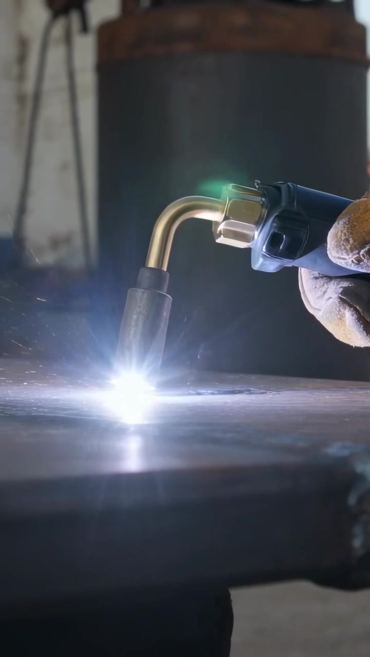 Vertical video: Touching steel plate gloved hand with torch making bead, sparks at bay, copy space