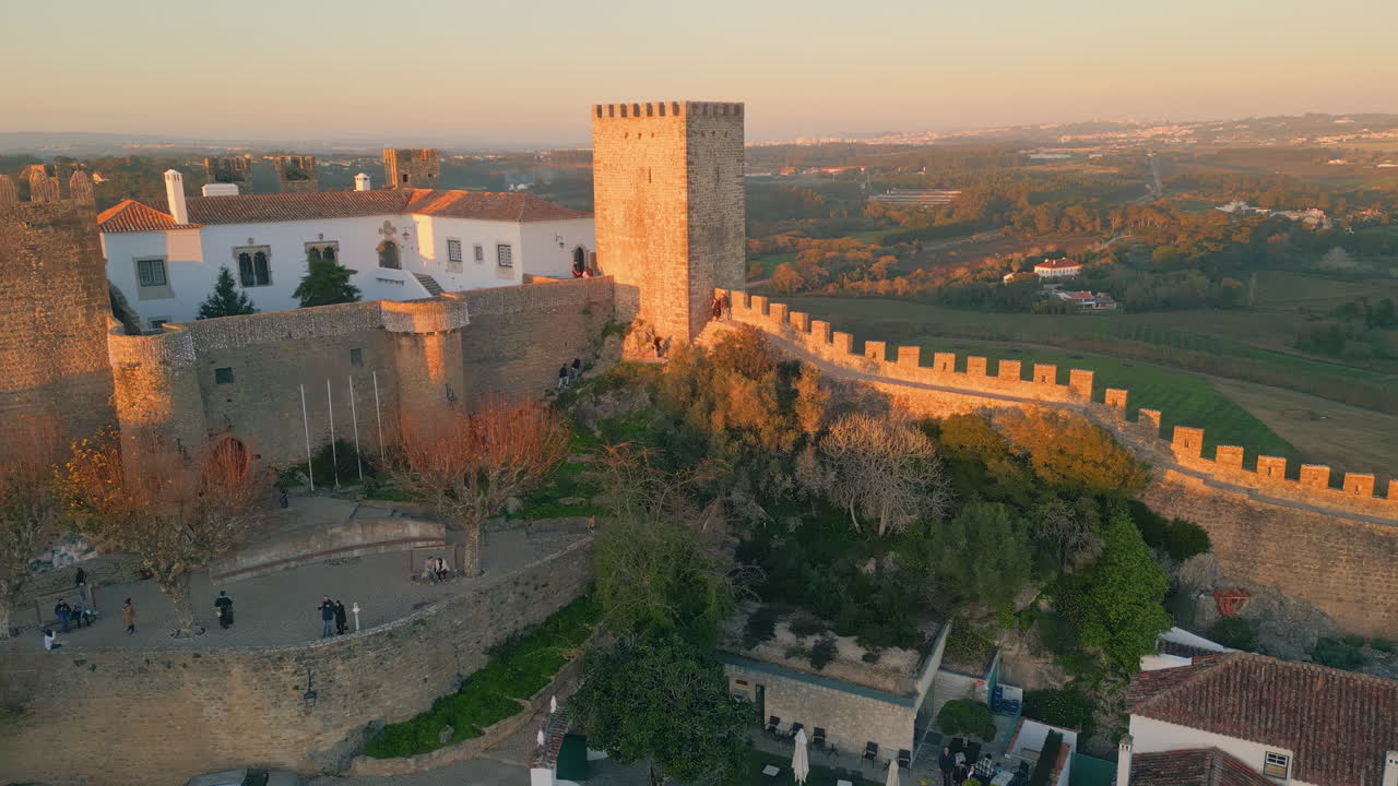 Sunset lighting castle stone towers rising over old village drone. Golden light