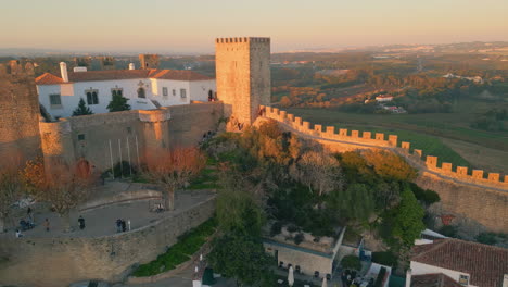 sunset lighting castle stone towers rising over old village drone. golden light