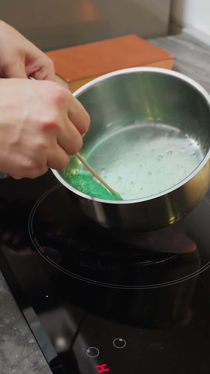 Partial view of person turning off electric stove while another person lifts pot with green liquid, stirring on induction stovetop, modern kitchen with kitchenware and cooking in action