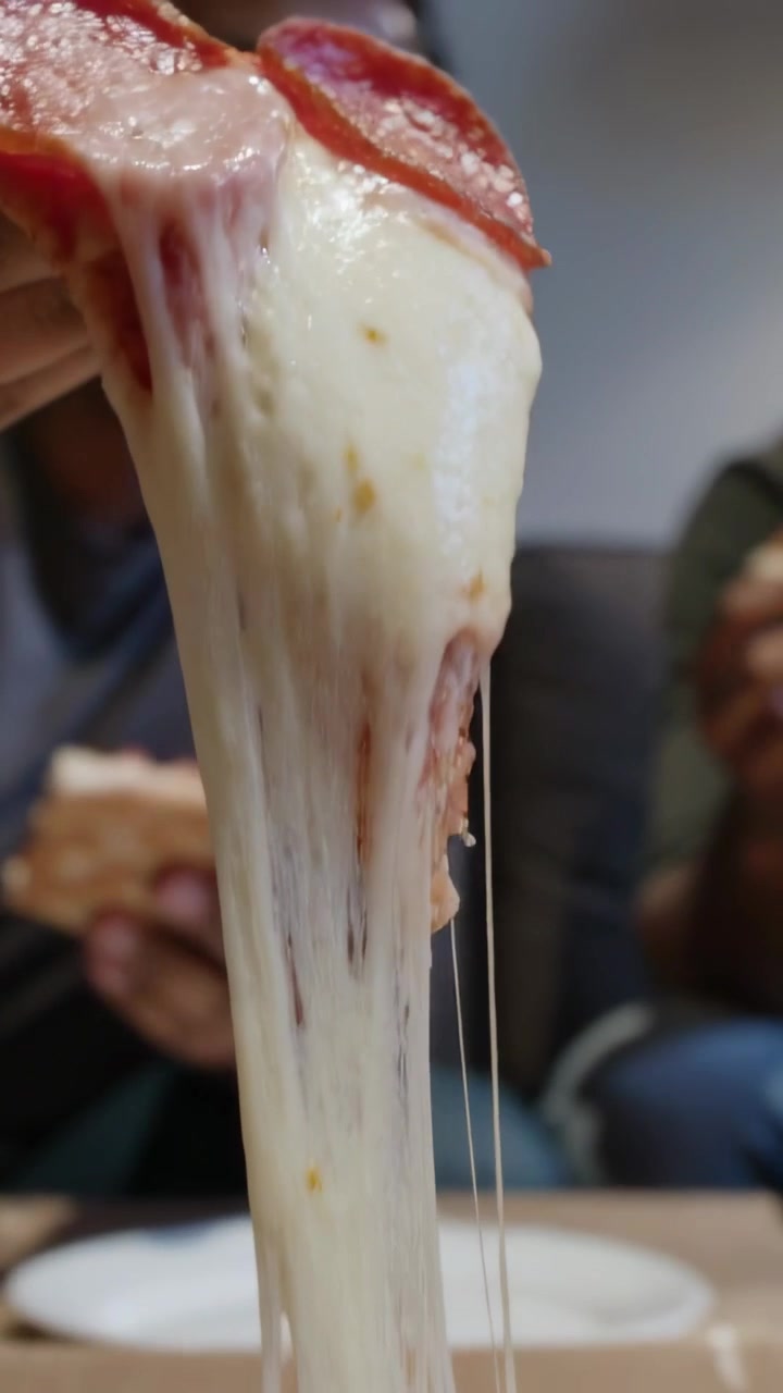 Video verticale: Uomo in maglietta che tira una fetta di salame piccante da una scatola di pizza a casa per mangiarla, con il formaggio che si allunga.